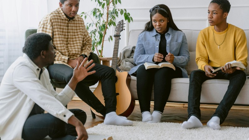 A group of four adults engaging in prayer and music indoors., tags: christliche jugend: glaube - pexel