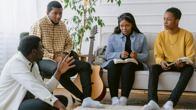 A group of four adults engaging in prayer and music indoors., tags: einer - pexel